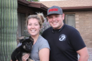 Smiling couple holding a small black dog.