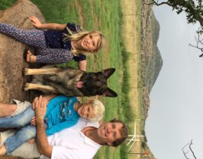 Family with German Shepherd outdoors, smiling together.
