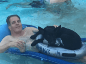 A man and his dog float in the pool.
