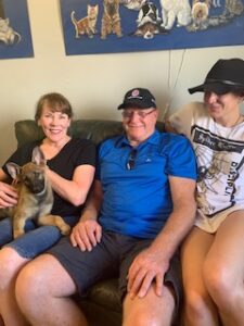 A man and two women sitting on the couch with their dog.