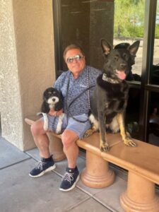A man and his dog sit on the bench outside.