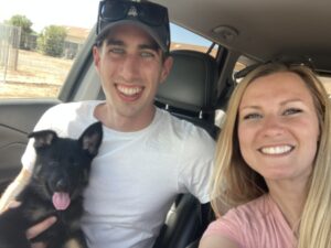 A man and woman in the back of a car with their dog.
